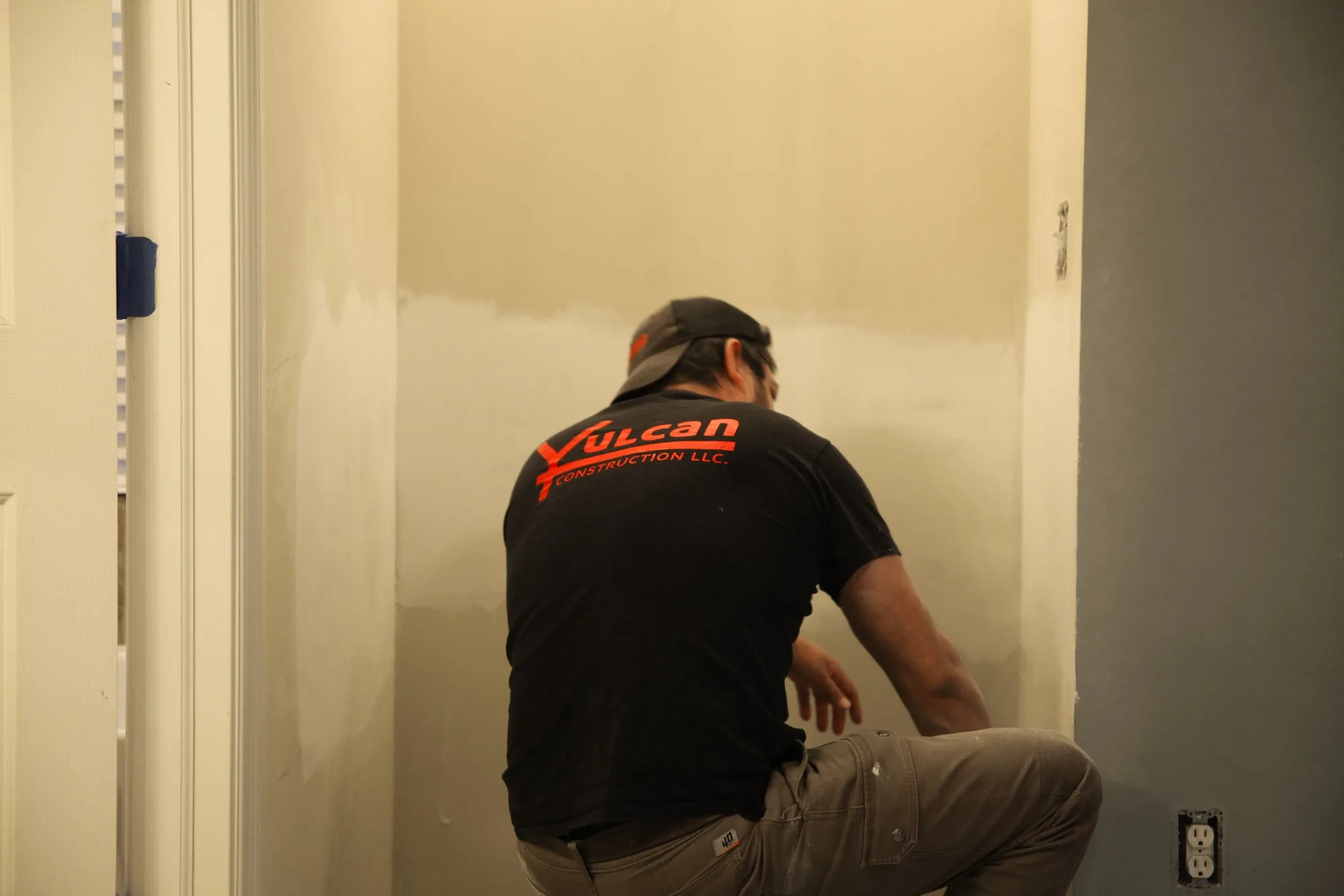 Vulcan worker patching and priming an interior wall