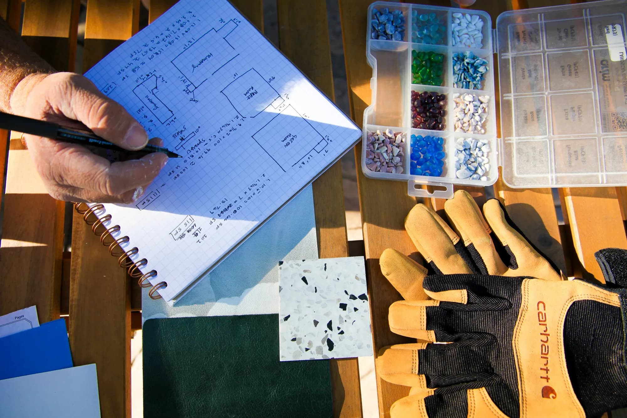 Hand-drawn floor plan beside tile, countertop and finish samples and work gloves