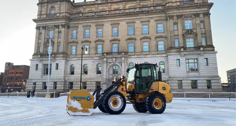 Wheel loader with a snow pusher in front of a historic stone building