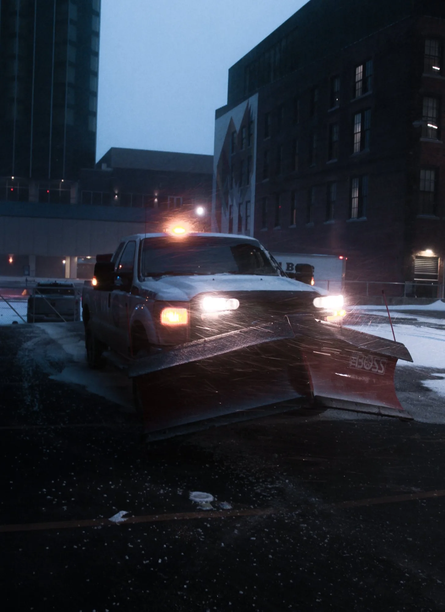 Pickup with a plow clearing a downtown street at dusk