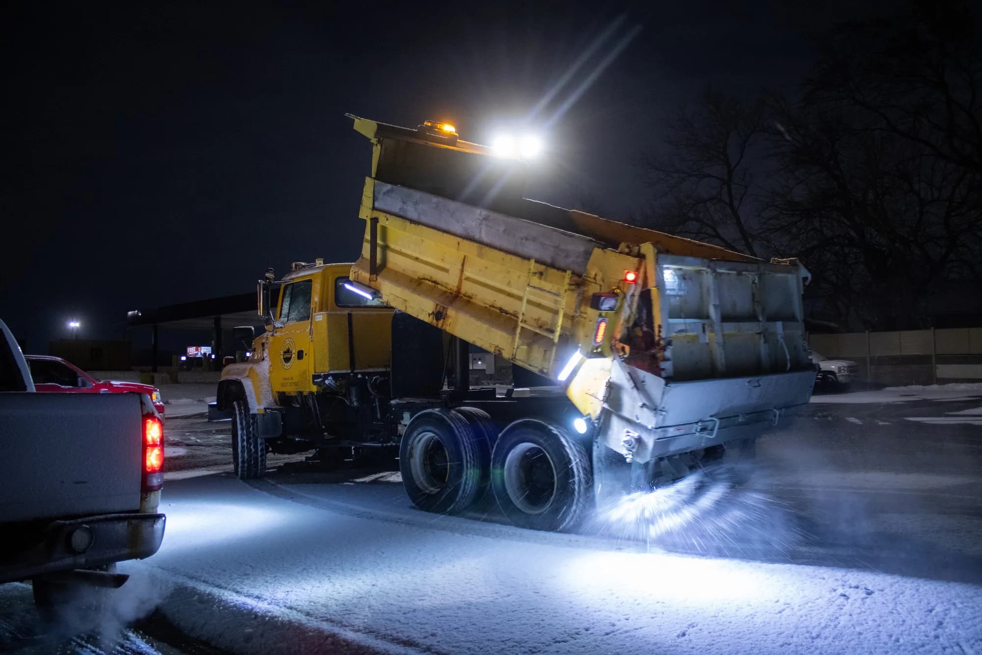Dump truck with its bed raised working a snowy lot at night
