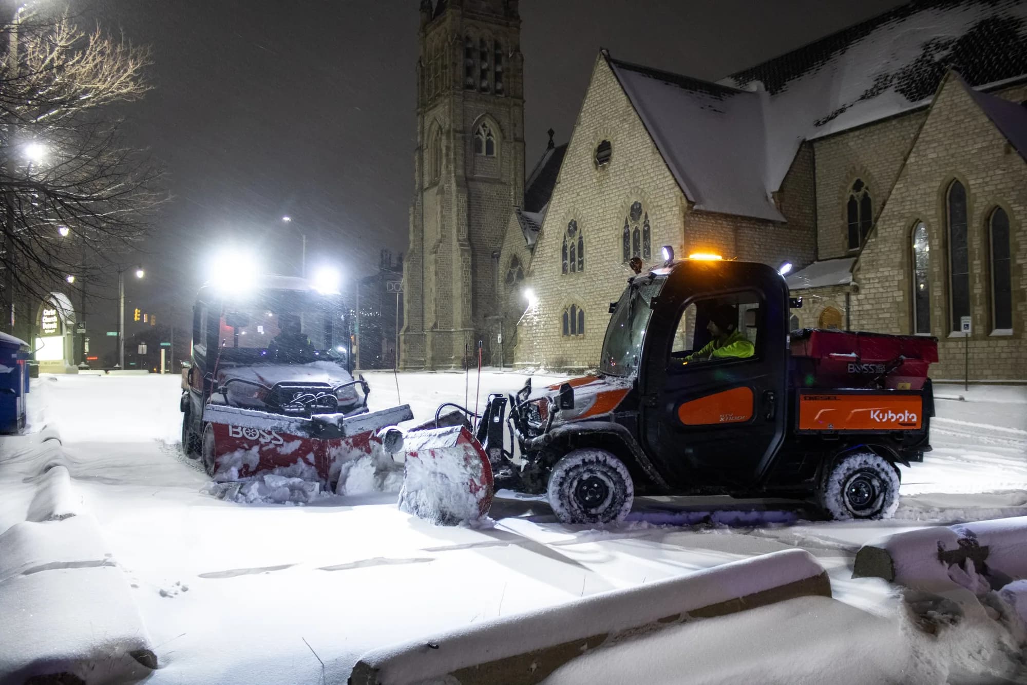 Utility vehicles with plows clearing snow beside a stone church