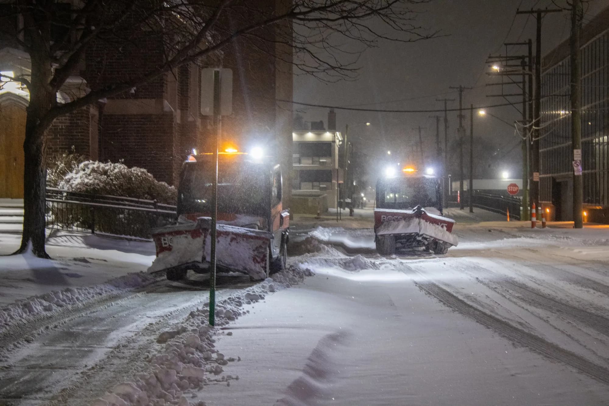 Utility vehicles with plows clearing a snowy street at night
