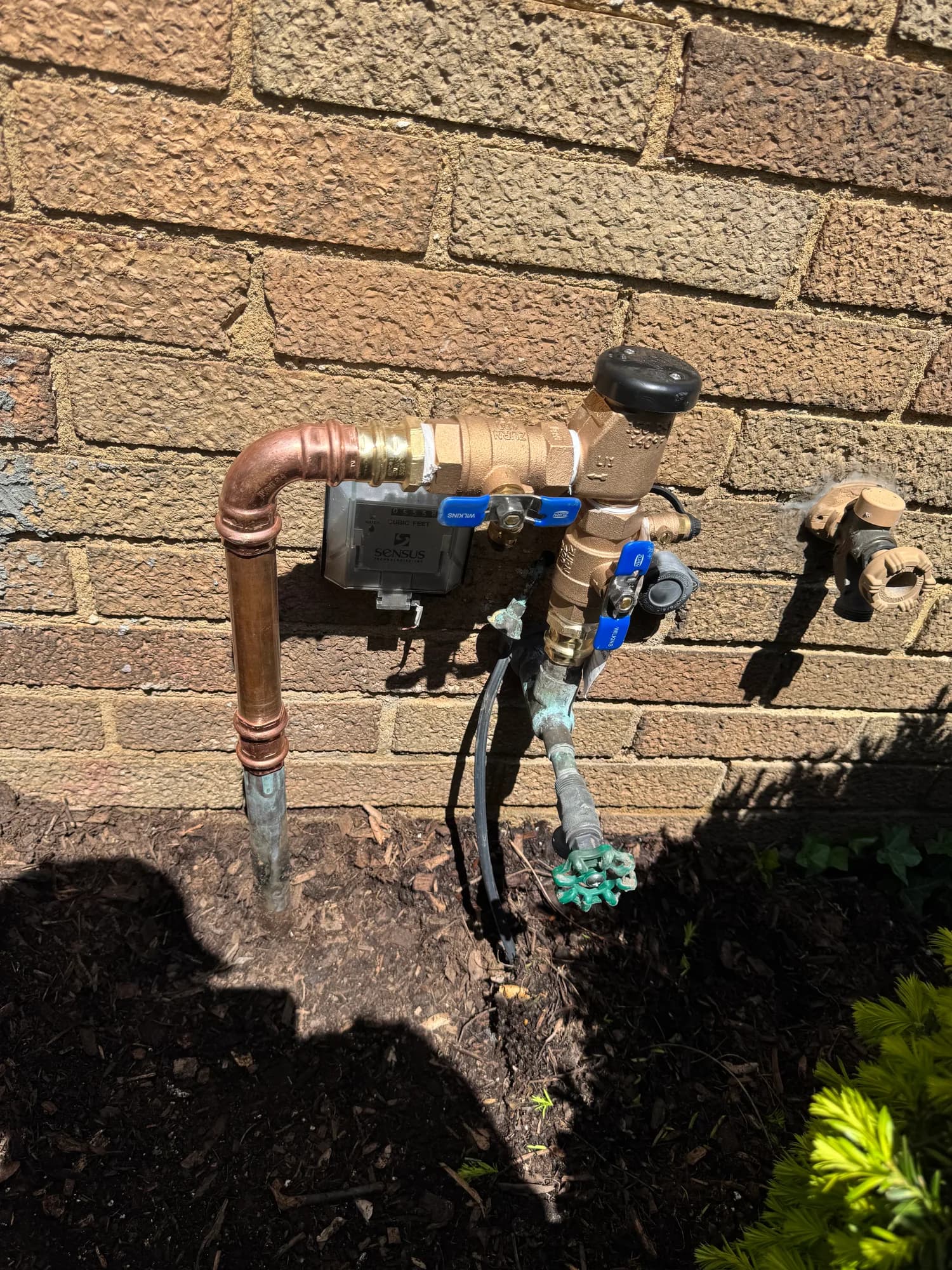 Copper irrigation backflow preventer installed against a brick wall