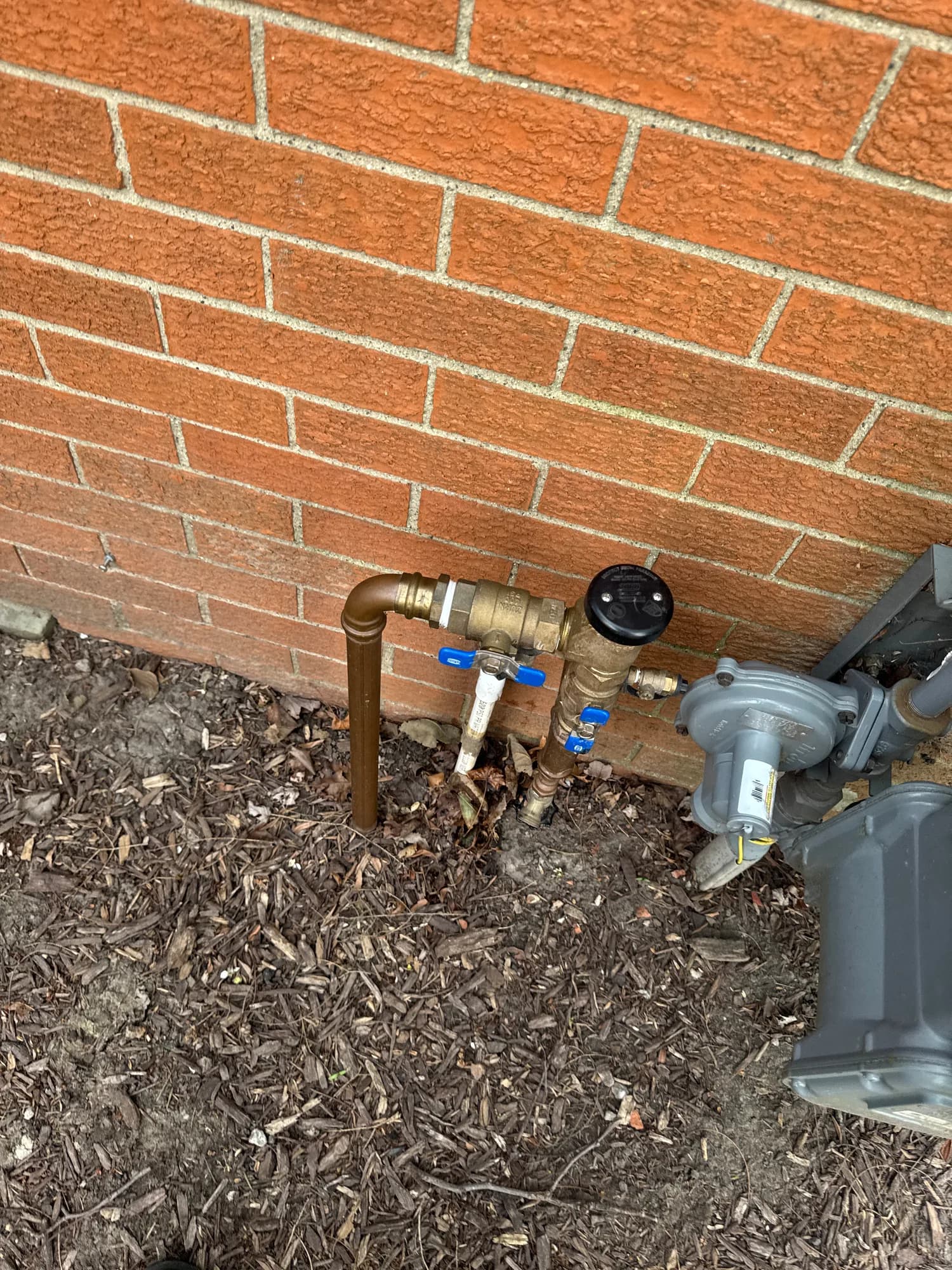 Backflow assembly on a brick house beside the gas meter