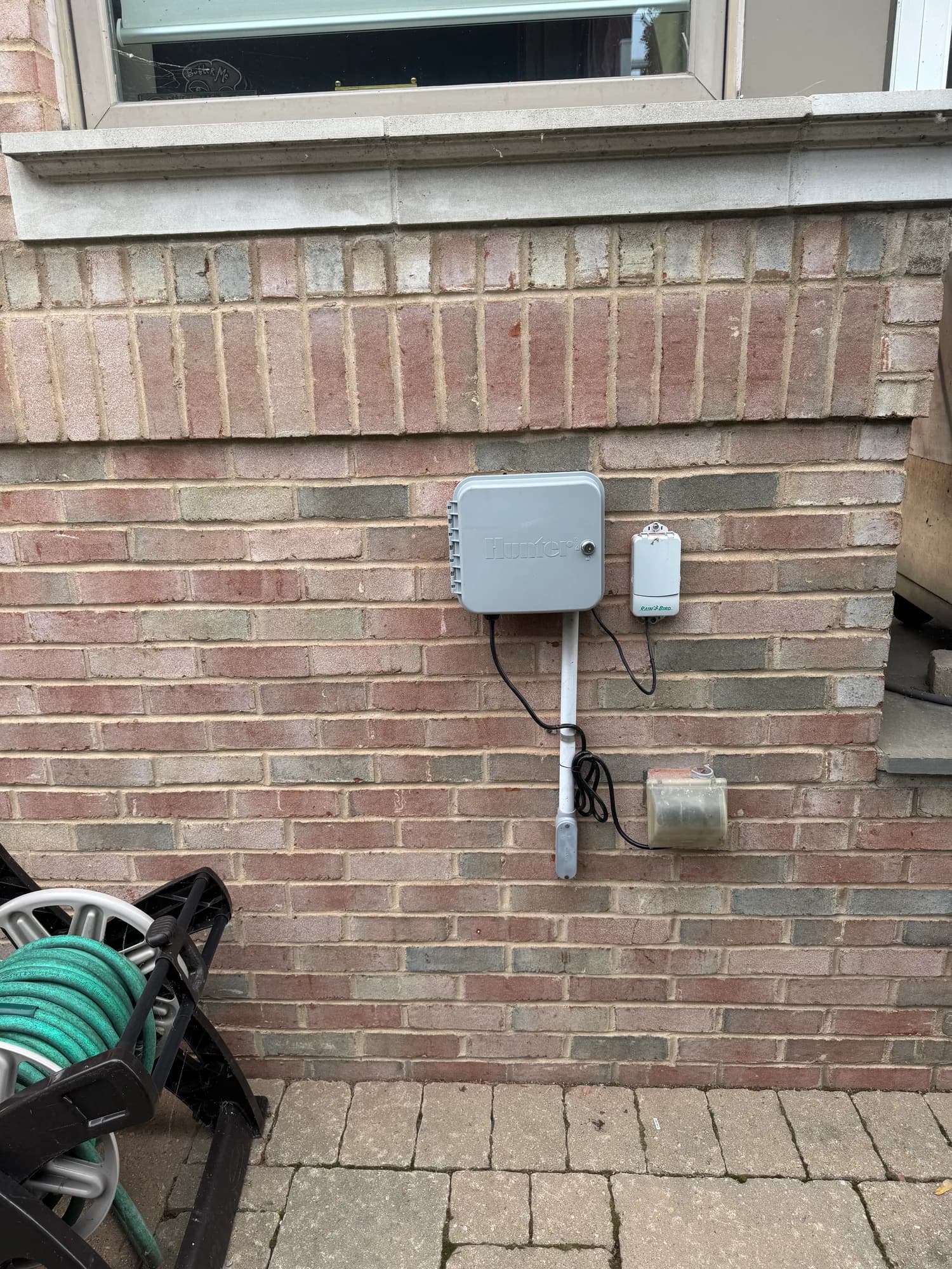 Sprinkler controller and wall-mounted sensor on a brick exterior