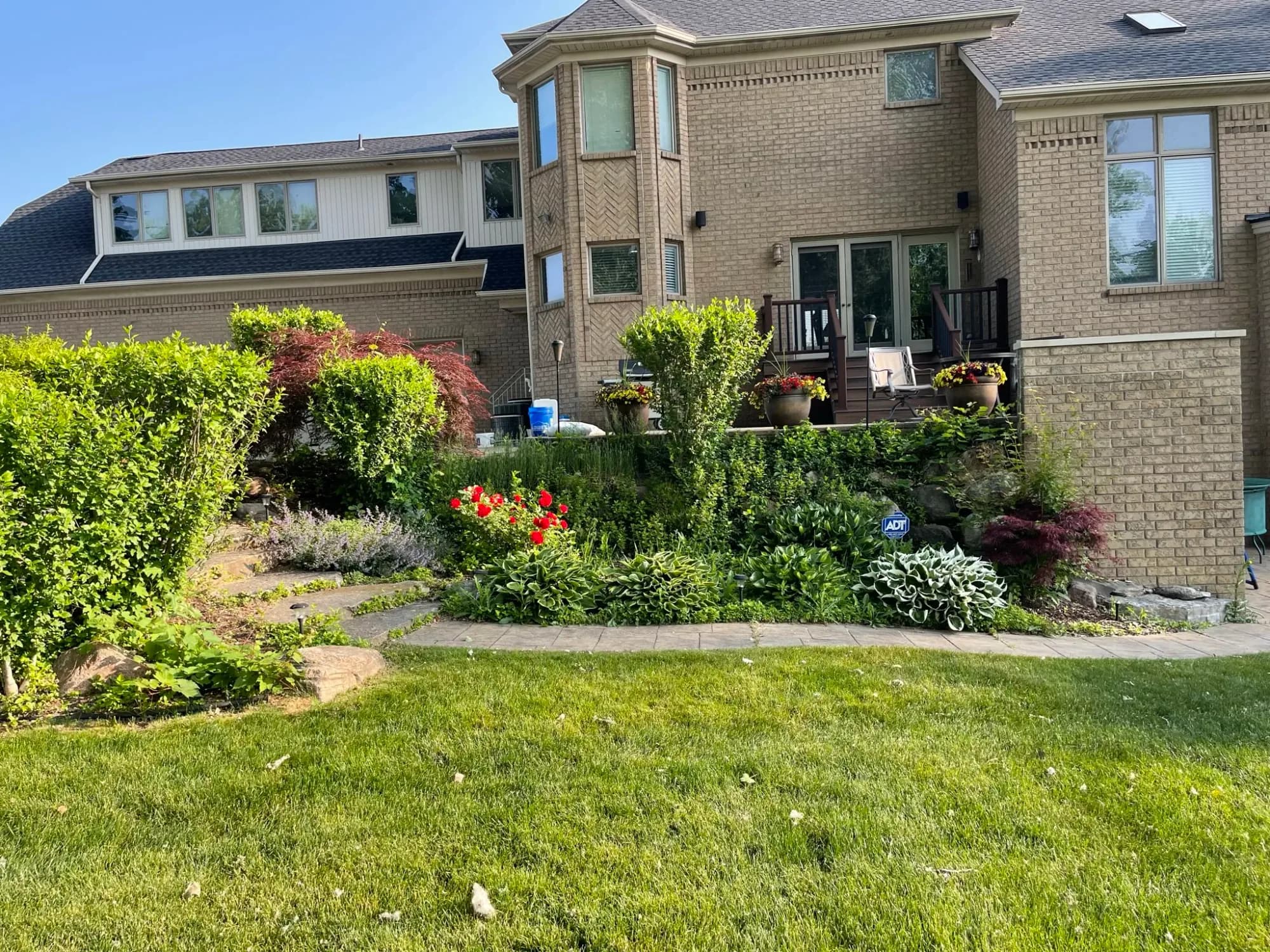 Backyard beds with flowering shrubs and perennials behind a brick house