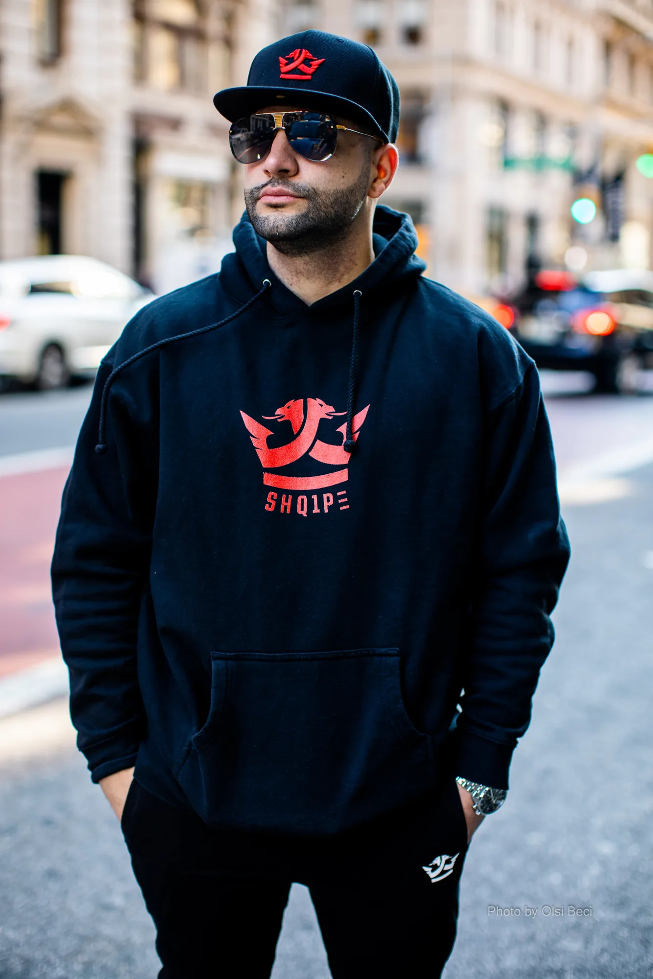 Man in a black hoodie with the red Shq1pe crown logo on a New York street