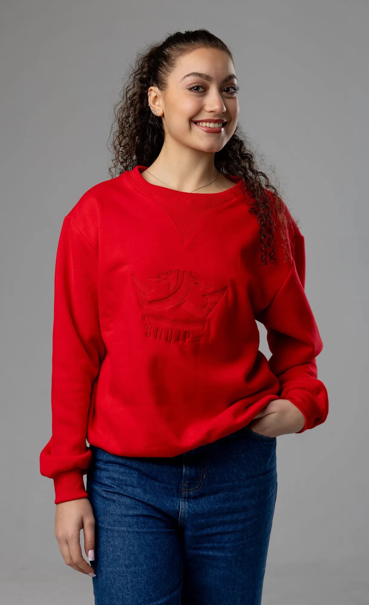 Woman in a red crewneck sweatshirt with an embossed logo