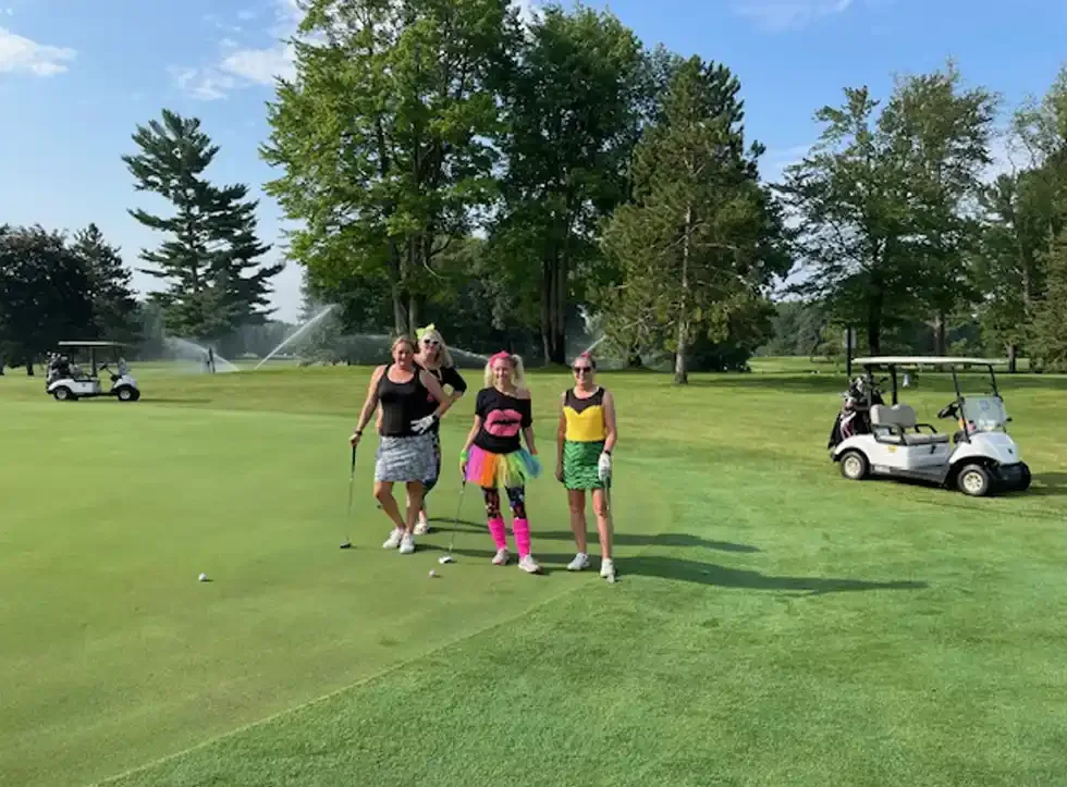 Golfers in colorful outfits on a fairway with carts behind them