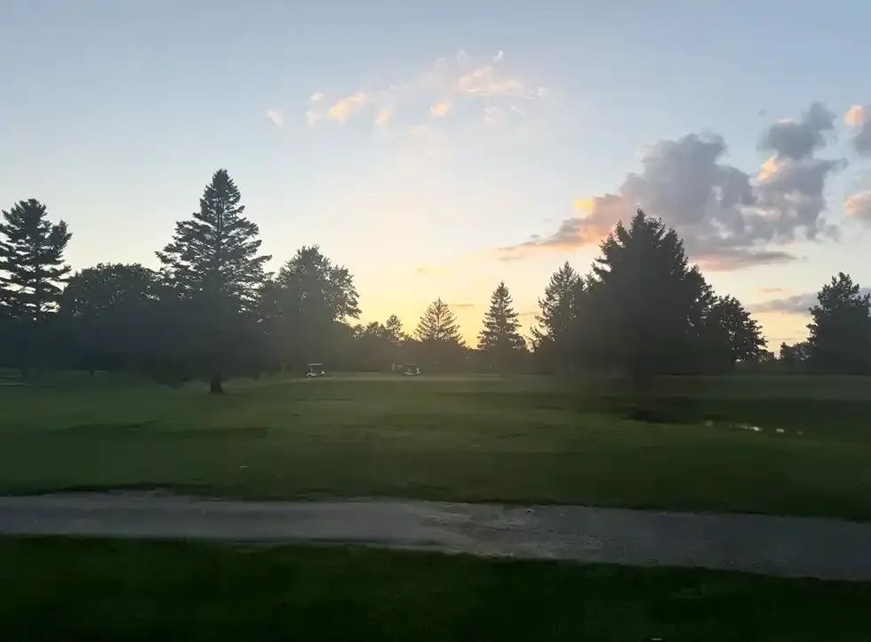 Low sun over the course and a stand of evergreens