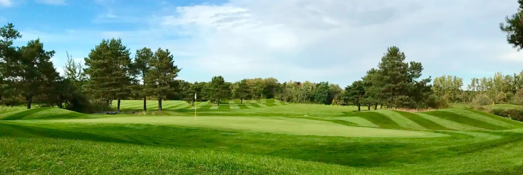 Wide striped fairway lined with evergreens