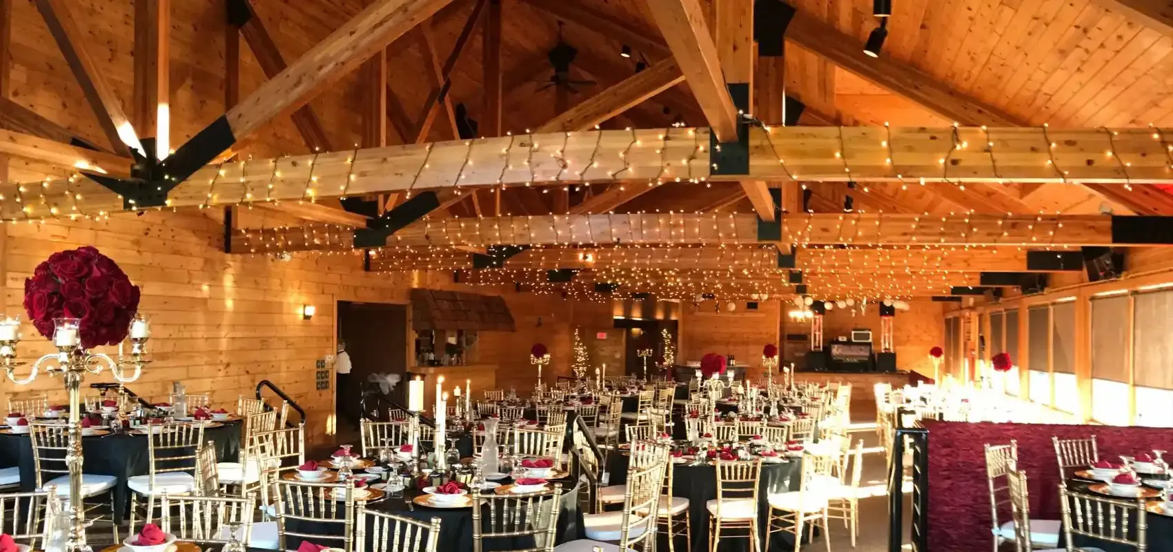 Wood-beamed banquet hall with string lights set for a reception